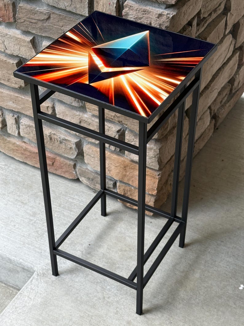 K&ouml;nnte beinhalten: Ein schwarzer Beistelltisch aus Metall mit quadratischer Oberseite. Die Tischplatte zeigt ein geometrisches Design mit orangefarbenen und blauen Lichtstreifen auf dunklem Hintergrund. Der Tisch hat ein minimalistisches Design.