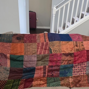 May include: A rectangular patchwork throw blanket featuring a variety of fabric squares in shades of deep red, burnt orange, forest green, navy blue, and brown. Each square displays distinct patterns including floral, paisley, and geometric motifs.