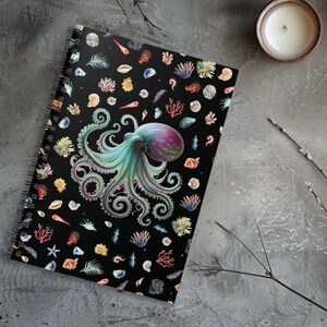 Puede incluir: Una libreta espiral negra con un patrón colorido de pulpo y conchas marinas. El pulpo es verde, morado y azul sobre un fondo negro.
