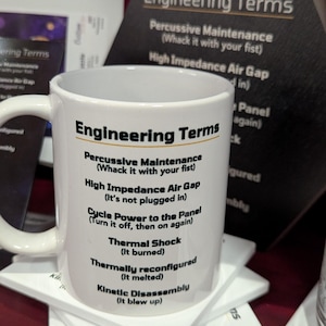 May include: A white ceramic mug featuring the black text Engineering Terms followed by a list of humorous definitions including Percussive Maintenance, High Impedance Air Gap, Cycle Power to the Panel, Thermal Shock, Thermally reconfigured, and Kinetic Disassembly.