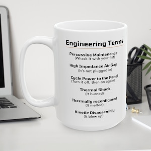 May include: White ceramic mug with a black and gold design. The mug features the text "Engineering Terms" and a list of humorous engineering terms with definitions.