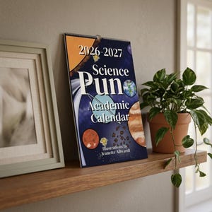 Op de afbeelding: Een 2026-2027 Science Pun academische kalender met een donkerblauwe ruimte-omslag met illustraties van planeten, sterren en asteroïden. De titel is gedrukt in witte en zwarte tekst, met vermelding van illustrator Jeanette Allwardt.