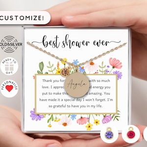 May include: A gold-colored necklace with a round pendant engraved with the name "Angela" is displayed in a gift box. The box is decorated with floral designs and the text "best shower ever". The box also includes a message.