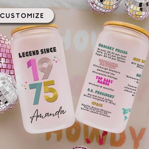 May include: Two frosted glass can-shaped tumblers with bamboo lids. One reads "LEGEND SINCE 1975 Amanda" in colorful text. The other lists 1975 events like grocery prices, Super Bowl, and space missions. The word "CUSTOMIZE" is at the top.