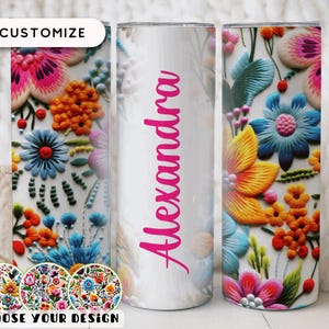 May include: A white tumbler with a floral design featuring pink, orange, blue, and yellow flowers. The word "Alexandra" is written vertically in pink. The tumbler is customizable and dishwasher safe.