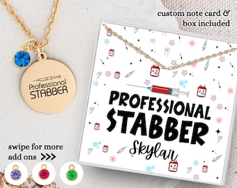 May include: Gold necklace with a round pendant that says "Professional Stabber" and a blue crystal charm. The necklace comes with a custom note card and box. The card has a white background with a red syringe, blood bags, and hearts. The text on the card says "Professional Stabber Skylar".