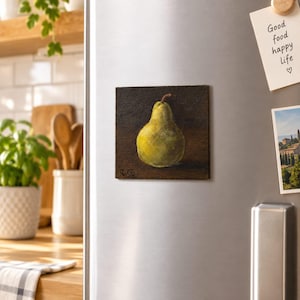 May include: A square refrigerator magnet featuring an oil painting of a single yellow-green pear centred against a dark, textured brown background. The artwork displays visible brushstrokes and includes the artist's initials R.G. in the bottom corner.