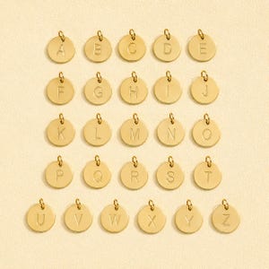 Puede incluir: Una colección de veintiséis dijes circulares de metal en tono dorado, cada uno con una letra mayúscula grabada del alfabeto de la A a la Z. Cada dije incluye una pequeña argolla en la parte superior para sujetarlo fácilmente a las joyas.