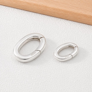 May include: Two oval-shaped spring gate rings in a polished silver tone. Each metal ring features a hinged opening mechanism and is stamped with the text 925 on the side, indicating the metal composition. The rings are smooth and metallic.