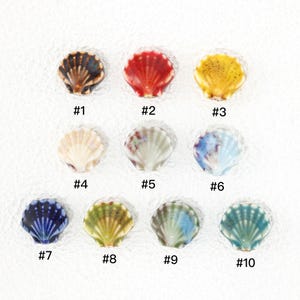 May include: Ten ceramic seashell-shaped beads arranged in three rows, labeled #1 through #10. The colors include dark brown, red, yellow, cream, white with green, blue and white, dark blue, olive green, light green, and teal with brown speckles.