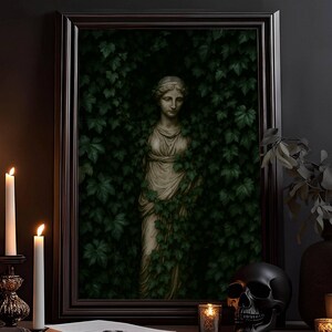 Könnte beinhalten: Ein gerahmter Druck einer klassischen Statue, umgeben von Efeu. Das Kunstwerk wird auf einer dunklen Oberfläche mit brennenden Kerzen, einem schwarzen Schädel und einem Buch präsentiert. Die Szene erinnert an eine gotische oder Vintage-Ästhetik.