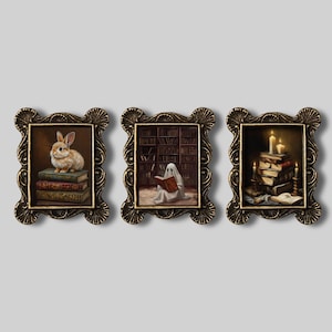 Pode incluir: Conjunto de três impressões de arte emolduradas com uma estética vintage. Cada moldura tem um acabamento dourado detalhado. As impressões retratam um coelho em livros, um fantasma lendo e velas com livros, tudo em uma paleta de cores quentes.