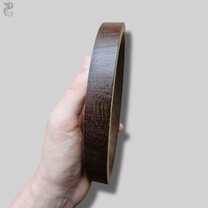 May include: A circular wooden frame with a dark brown stained finish and a visible wood grain texture. The object has a smooth, rounded outer edge and a flat inner surface, showcasing a deep, rich color profile throughout the entire structure.