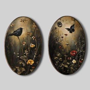 Op de afbeelding: Twee ovale wandkunstwerken. Eén toont een zwarte vogel op een tak met gele bloemen. De andere toont een vlinder en rode bloemen. Beide hebben een donkere, rustieke achtergrond.