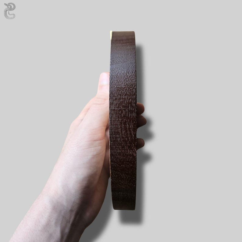 May include: A circular object with a dark brown, textured wooden surface viewed from the side. The item has a smooth, flat edge and a visible wood grain pattern throughout its exterior, showcasing a deep, rich brown color and a solid, sturdy construction.