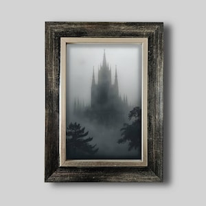 Könnte beinhalten: Ein gerahmter Druck mit einem gotischen Schloss in einer nebligen Landschaft. Das Bild ist überwiegend in Grau- und Schwarztönen gehalten, wobei die Türme und Türmchen des Schlosses durch den Nebel sichtbar sind. Der Rahmen ist dunkel mit einem metallischen Innenrand.