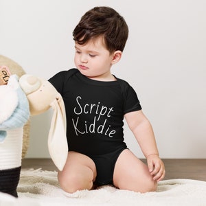 May include: A baby wearing a black bodysuit with the text "Script Kiddie" in white lettering. The baby is sitting on a white fluffy surface and looking down at a stuffed animal.