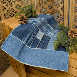 Pu&ograve; includere: Una tovaglia in denim con un design patchwork in varie tonalit&agrave; di blu. La tovaglia &egrave; rettangolare con un bordo sfilacciato. La tovaglia &egrave; decorata con pigne e rami sempreverdi.