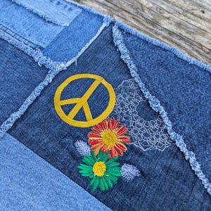 May include: A denim patchwork fabric with a yellow peace sign and embroidered flowers in red, yellow, and green.