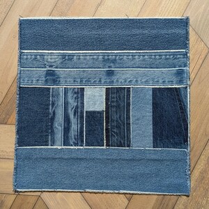 Pu&ograve; includere: Tessuto patchwork quadrato in denim. Il tessuto &egrave; realizzato con varie tonalit&agrave; di denim blu, disposte a strisce orizzontali e verticali. I bordi sono sfilacciati e il pezzo &egrave; appoggiato su una superficie di legno.