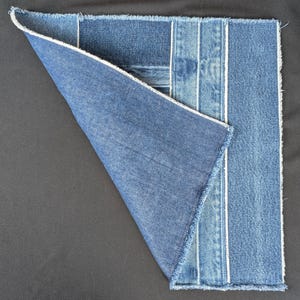 Pu&ograve; includere: Un pezzo quadrato di tessuto denim con un angolo piegato, che mostra varie tonalit&agrave; di denim blu. Il design incorpora strisce verticali con cuciture bianche e una finitura a bordo grezzo. L'angolo piegato rivela l'interno del tessuto.