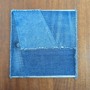 May include: A blue denim patchwork coaster with frayed edges. The coaster is made of two different shades of blue denim, sewn together in a geometric pattern.