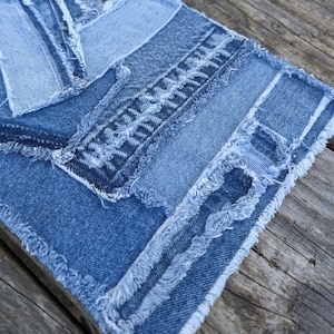 May include: A close-up of a blue denim patchwork wall hanging with frayed edges. The denim is arranged in a layered pattern with different shades of blue.