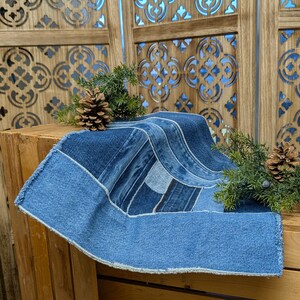 Pu&ograve; includere: Runner da tavolo in denim patchwork in varie tonalit&agrave; di blu. Il runner &egrave; rettangolare con un bordo sfilacciato e un design geometrico. Decorato con pigne e rametti sempreverdi, creando un'estetica rustica.