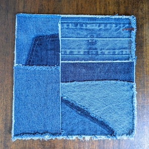 May include: A blue denim patchwork coaster with frayed edges. The coaster is made of different shades of blue denim and has a variety of textures.