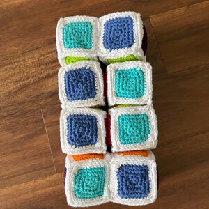 May include: A set of six colorful crocheted blocks with white borders. Each block features a different color in the center, including blue, green, orange, and red.