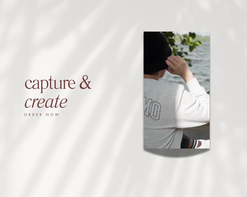 May include: A white long-sleeve shirt with the word "MO" printed on the back. The person is wearing a black knit hat and is standing by a body of water.