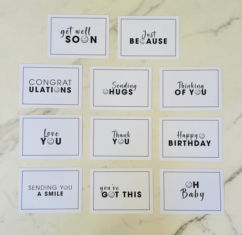 May include: Twelve white cards with black text and smiley faces. The cards have messages such as "Get Well Soon", "Just Because", "Thinking of You", "Happy Birthday", "Love You", "Sending Hugs", "You've Got This", "Oh Baby", "Sending You a Smile", "Congratulations", and "Thank You".