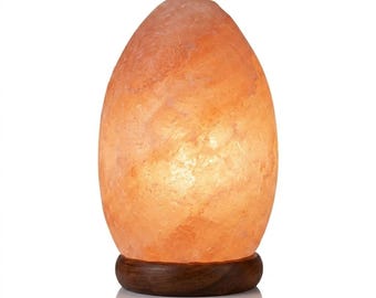 May include: A Himalayan salt lamp with a warm orange glow. The lamp has an egg-like shape and sits on a dark brown wooden base. The surface of the salt lamp has a textured appearance, and the light emanates from within.