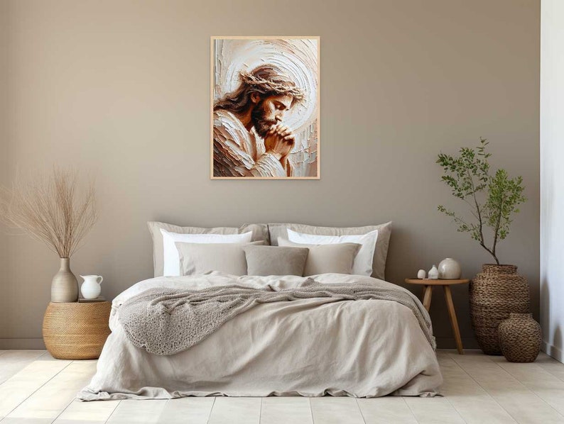May include: A painting of Jesus Christ with a crown of thorns, praying with his hands clasped together. The painting is in a light brown frame and is hanging on a beige wall.