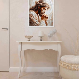 May include: A painting of Jesus Christ with a crown of thorns, praying with his hands clasped together. The painting is in a white frame and is hanging on a white wall.