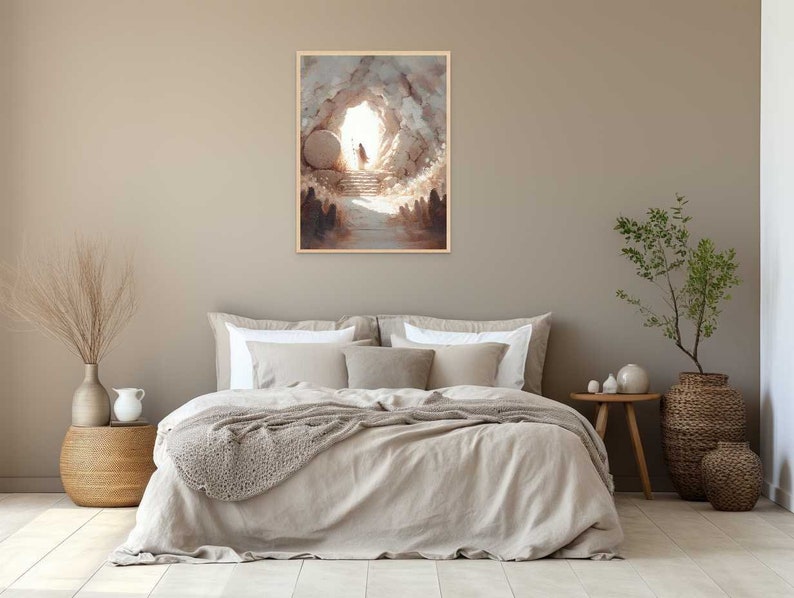 Puede incluir: Una pintura que representa la apertura de una cueva con una gran piedra rodada, revelando una luz brillante y una figura caminando hacia ella. La pintura est&aacute; enmarcada y colgada en una pared sobre una cama con un edred&oacute;n de lino beige.