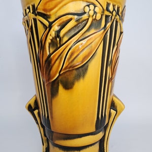 May include: A yellow ceramic vase with a floral design. The vase has a wide mouth and a narrow base. It is decorated with a brown and black floral pattern.