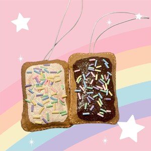 May include: Two felt ornaments shaped like pop-tart pastries. One is frosted with white and has pastel sprinkles. The other is frosted with chocolate and has pastel sprinkles.