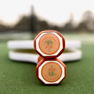 Two pickleball paddles laying on a pickleball court, showing the end cap of the handles which features the Paddle and Palm logo.