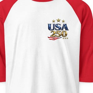 May include: White baseball style shirt with red sleeves. The shirt features the text "USA 250" with stars and stripes graphic on the front. A casual, patriotic tee.