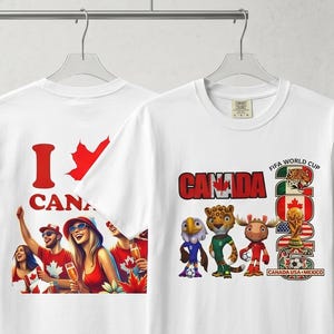 Op de afbeelding: Twee witte T-shirts met Canada-thema's hangen aan een metalen rek. E&eacute;n shirt toont "I Canada" met een esdoornblad, de andere toont "Canada" met FIFA Wereldbeker-afbeeldingen. Een rood-witte voetbal en een keepershandschoen maken de presentatie compleet.