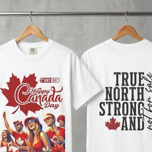 May include: White t-shirts with Canada Day graphics. One shirt features a red maple leaf and the text "Happy Canada Day" with a graphic of people celebrating. The other shirt has "True North Strong and" text.