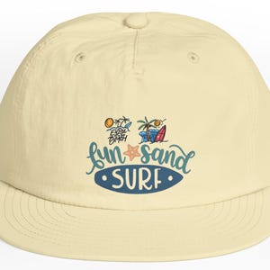 Op de afbeelding: Lichtbeige baseballpet met een gebogen klep. De pet heeft een kleurrijke afbeelding met de woorden "fun sand surf" en afbeeldingen van een palmboom, surfplank en zeester. Een casual accessoire.