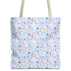 May include: A light blue tote bag with a floral pattern featuring pink, white, and yellow flowers, and green leaves. The bag has beige handles and is designed for carrying items. The overall design is a floral theme.