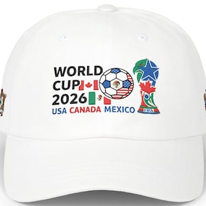 May include: White baseball cap featuring the text "WORLD CUP 2026" with flags of USA, Canada, and Mexico. A soccer ball graphic and the FIFA trophy are also displayed. The cap has a curved brim.
