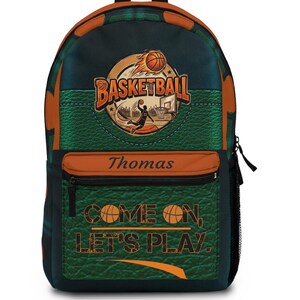May include: A backpack featuring a basketball theme with a green textured background and orange accents. The front displays a basketball graphic, the text "BASKETBALL", the name "Thomas", and the phrase "COME ON, LET'S PLAY." with basketball icons.