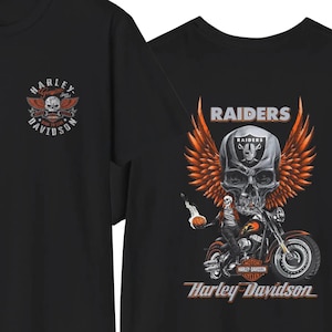 K&ouml;nnte beinhalten: Ein schwarzes T-Shirt mit einem kleinen Harley-Davidson-Logo auf der Brust. Die R&uuml;ckseite zeigt eine gro&szlig;e Grafik eines Totenkopfes mit orangefarbenen Fl&uuml;geln, einem Motorrad und dem Schriftzug Raiders und Harley-Davidson in Wei&szlig; und Orange.