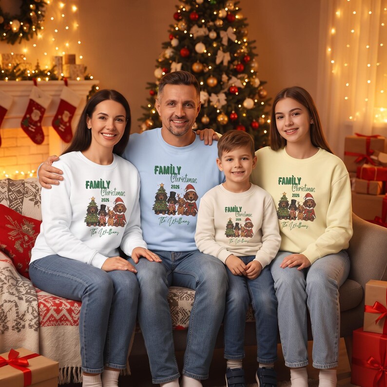 K&ouml;nnte beinhalten: Vier lang&auml;rmelige Rundhals-Sweatshirts in Wei&szlig;, Hellblau, Beige und Hellgelb. Jedes zeigt eine Grafik von vier Hunden in festlicher Kleidung, den Text "Family Christmas 2026" und den Namen "The Williams" auf der Vorderseite aufgedruckt.