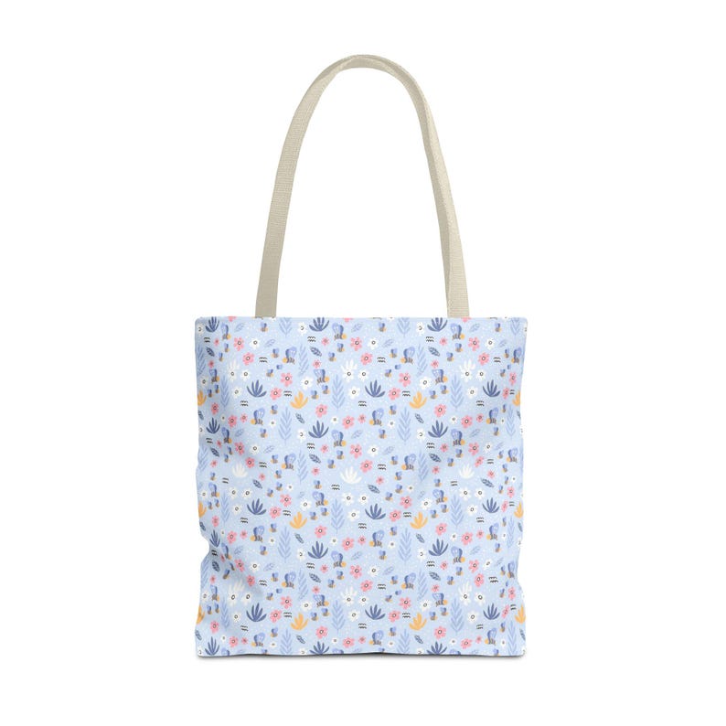 May include: A light blue tote bag with a floral pattern featuring pink, white, and yellow flowers, and green leaves. The bag has beige handles and is designed for carrying items. The overall design is a floral theme.
