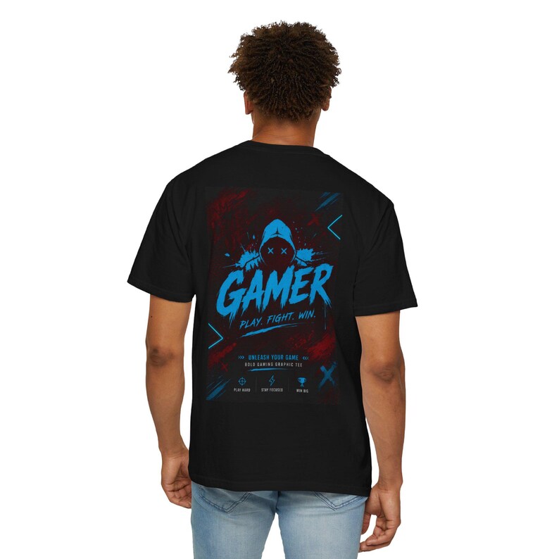 May include: A black short-sleeve t-shirt featuring a back graphic with a hooded figure, the text GAMER PLAY. FIGHT. WIN., UNLEASH YOUR GAME, BOLD GAMING GRAPHIC TEE, and icons for play hard, stay focused, and win big in blue and red colors.
